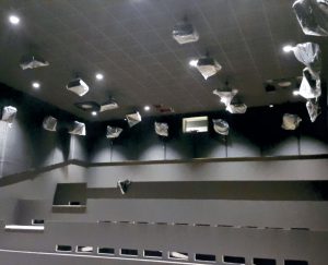 Et udsnit af højttalerne i en af de mindste sale og desuden kan anes begge subwoofere, der er monteret i loftet over bagerste række.